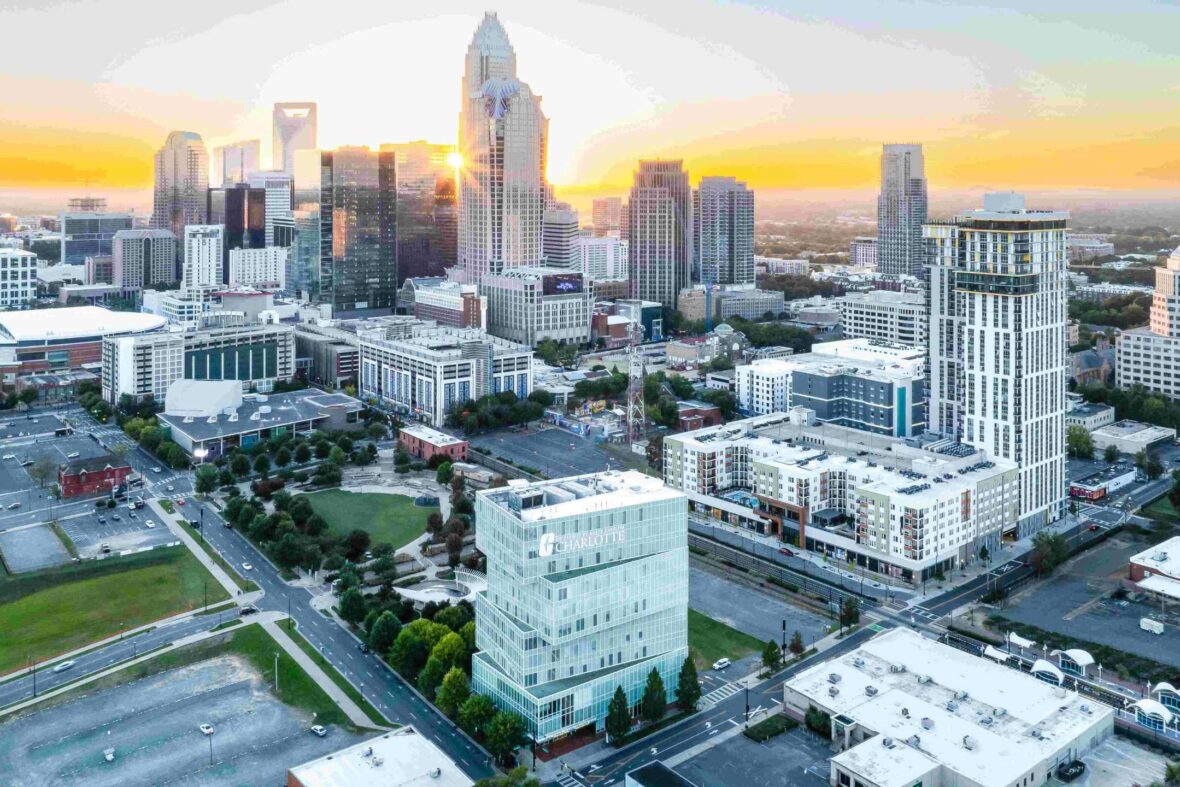 Cityscape view at sunrise with diverse architectural skyline and a UNC Charlotte building in the foreground.