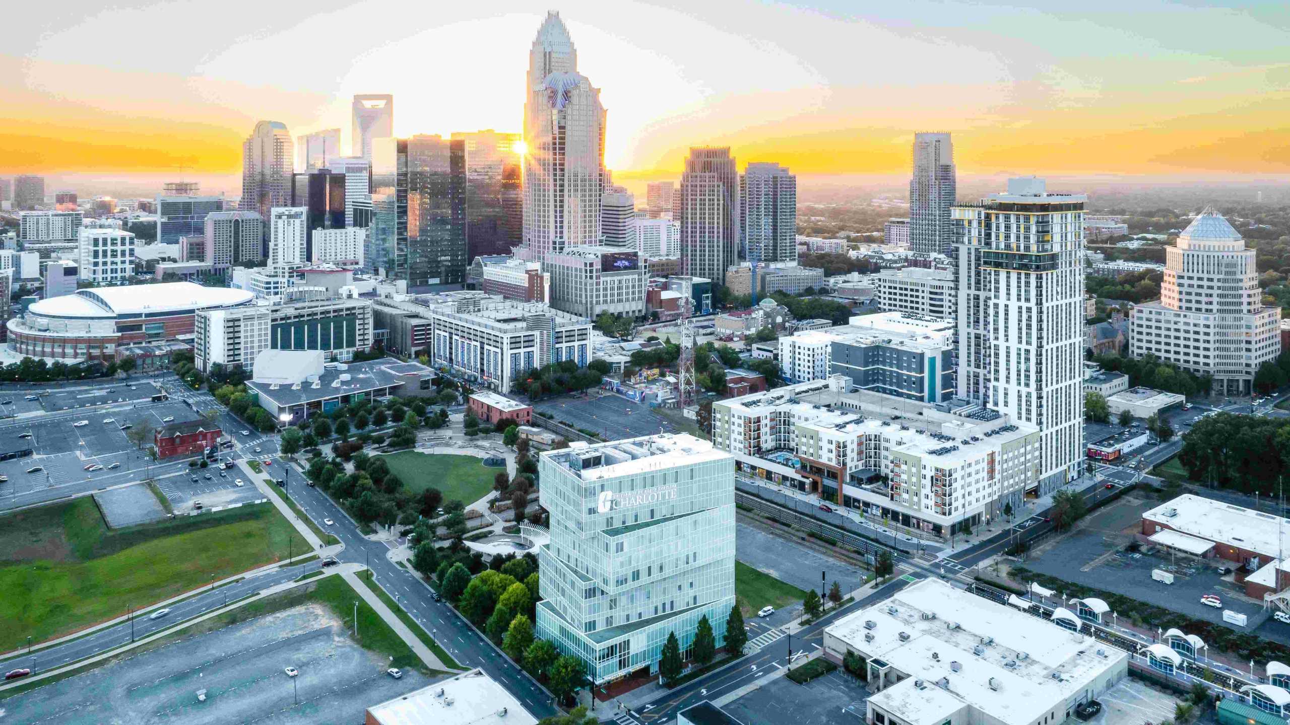 Cityscape view at sunrise with diverse architectural skyline and a UNC Charlotte building in the foreground.